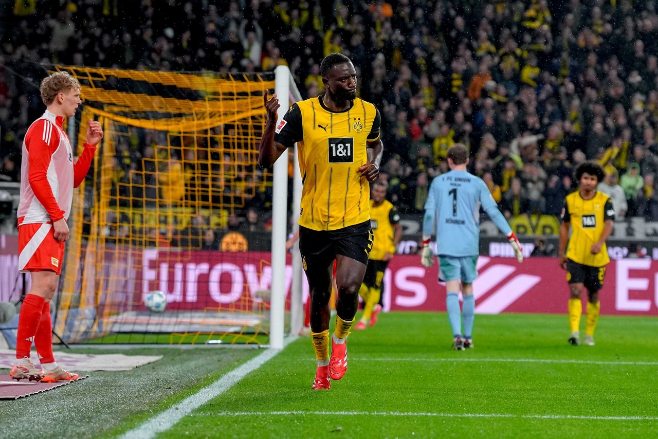 Borussia Dortmunds Stürmer Serhou Guirassy läuft jubelnd an der Torauslinie entlang. Berlins Reservespieler Leopold Querfeld schaut konsterniert.