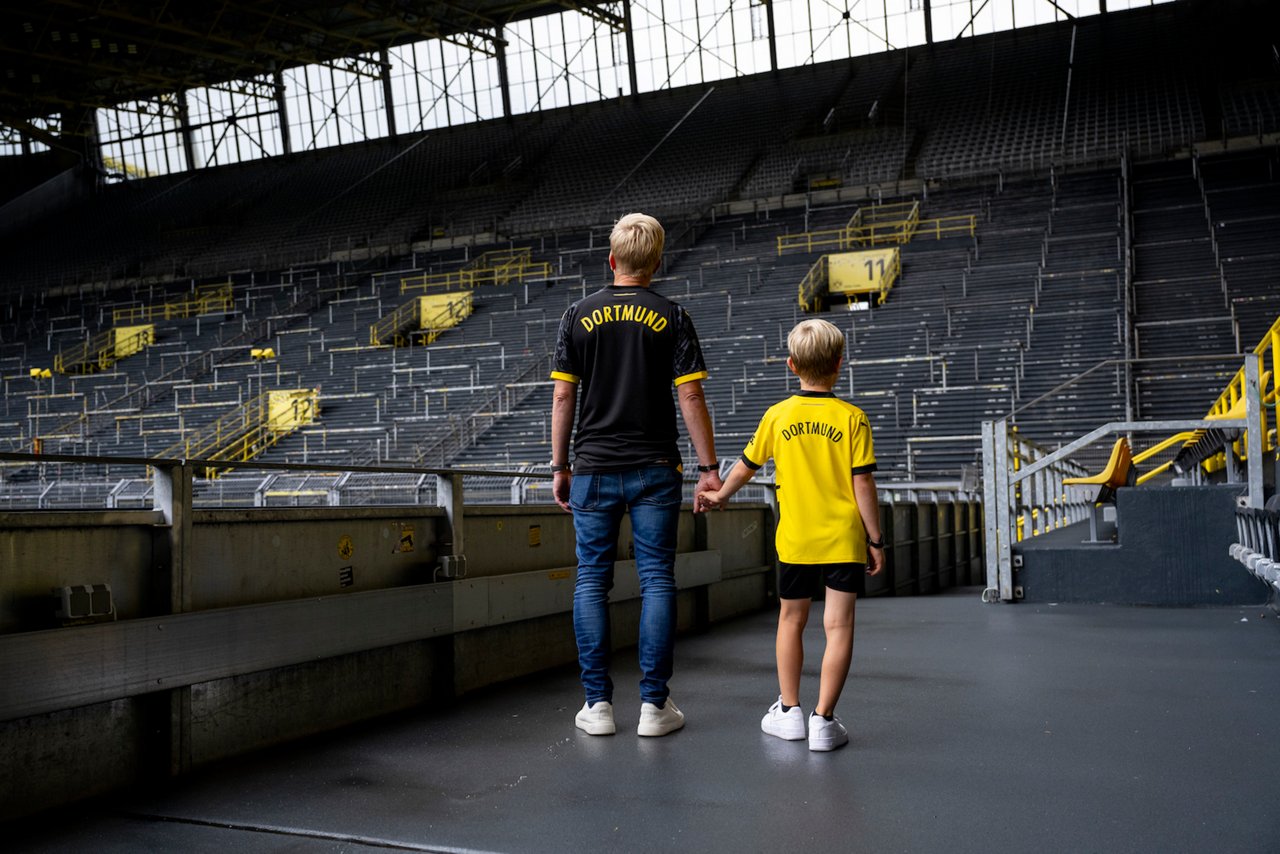 Mann läuft mit seinem Kind an der Hand durch das leere Stadion