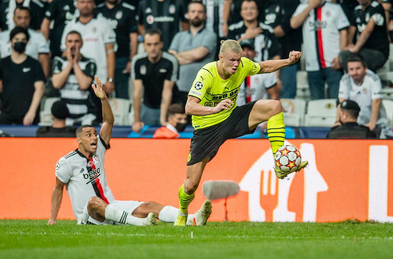 Erling Haaland nimmt einen Ball mit dem linken Fuß an. Hinter ihm reklamiert ein Besiktas-Spieler auf dem Boden sitzend ein Foul.