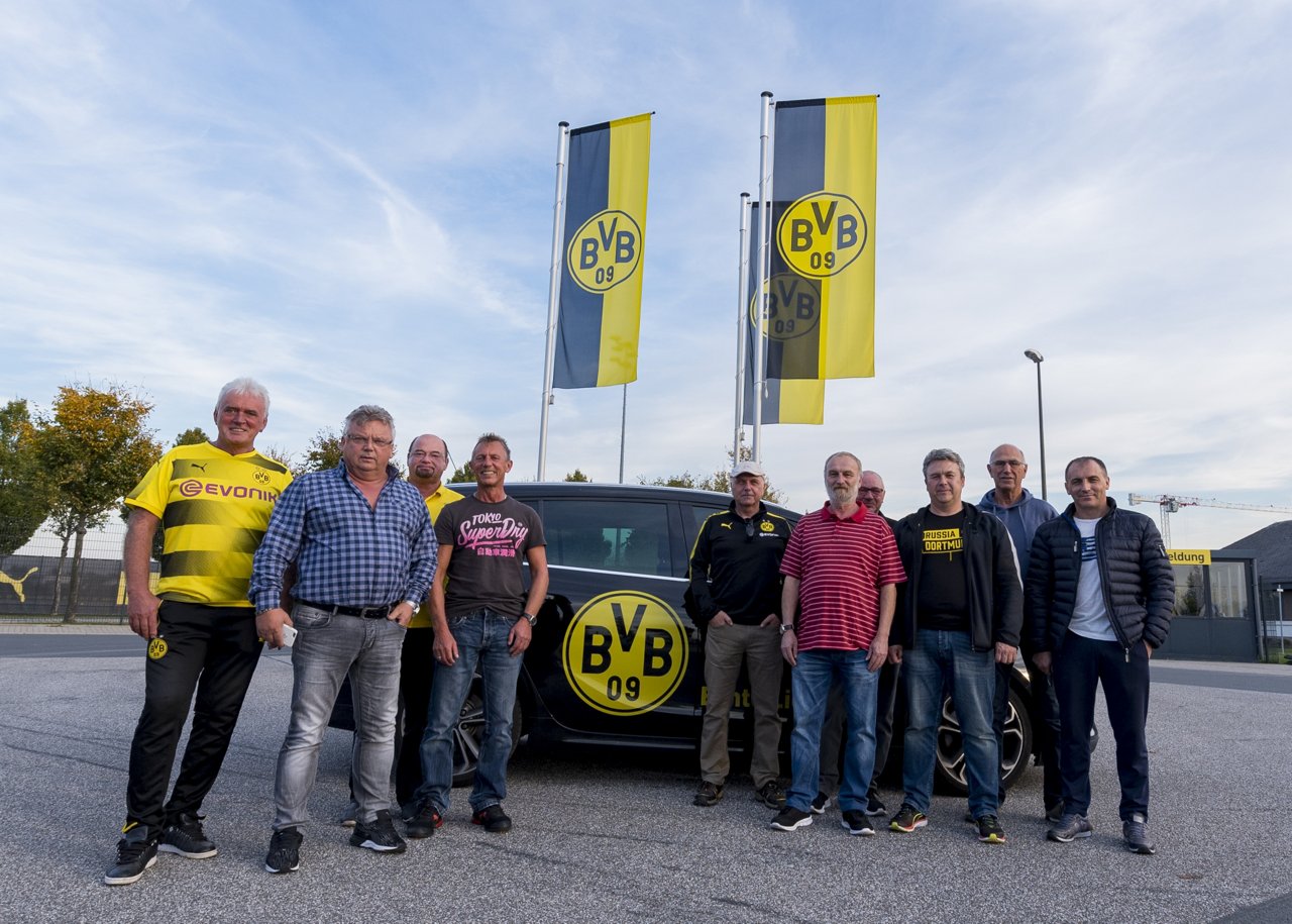 Mitarbeiter des Fahrdienstes stehen vor dem für den Fahrdienst verwendeten Auto.