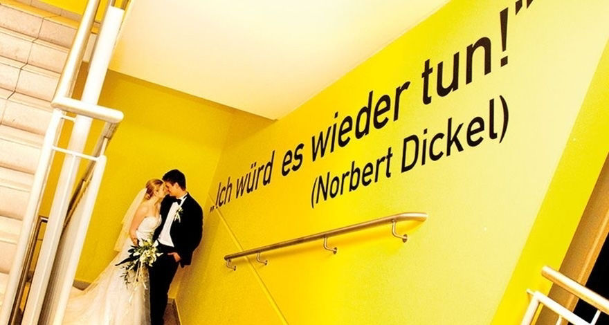 Hochzeitspaar vor einer gelben Wand mit einem Zitat von Norbert Dickel