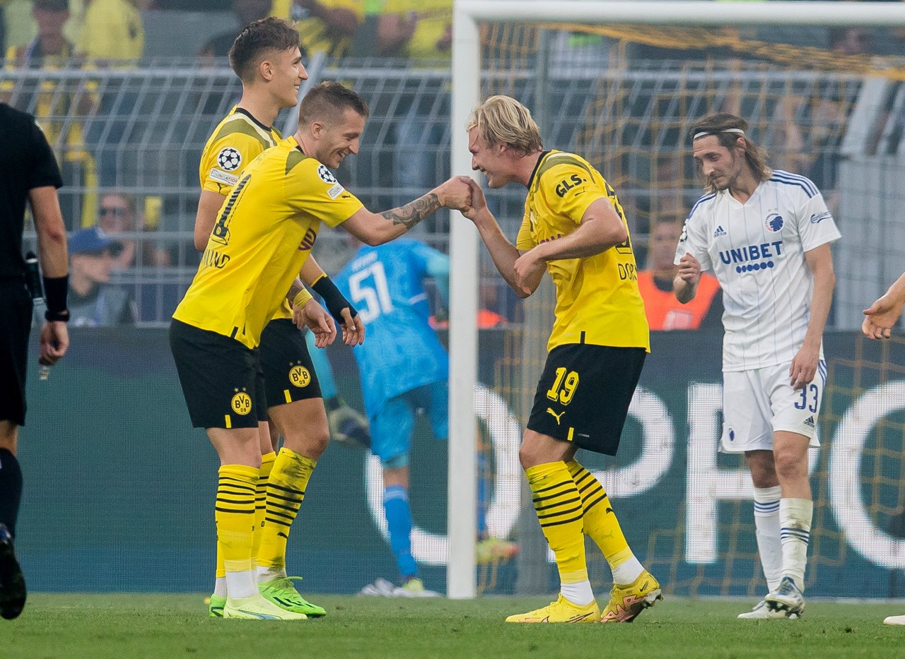 Marco Reus und Julian Brandt geben sich auf dem Platz lachend die Hand.