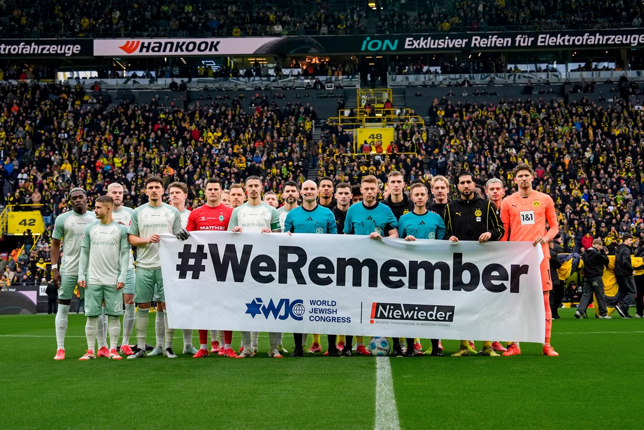 Spieler von Werder Bremen und Borussia Dortmund sowie die Schiedsrichter halten ein Banner mit der Aufschrift "#WeRemember" im Stadion in die Höhe.