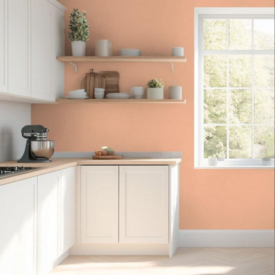 Kitchen with Valspar Mellow Mango painted walls in a warm peach tone, featuring white cabinets, wooden worktops, open shelving styled with ceramics and plants, and a large window bringing in natural light for a bright, welcoming feel.