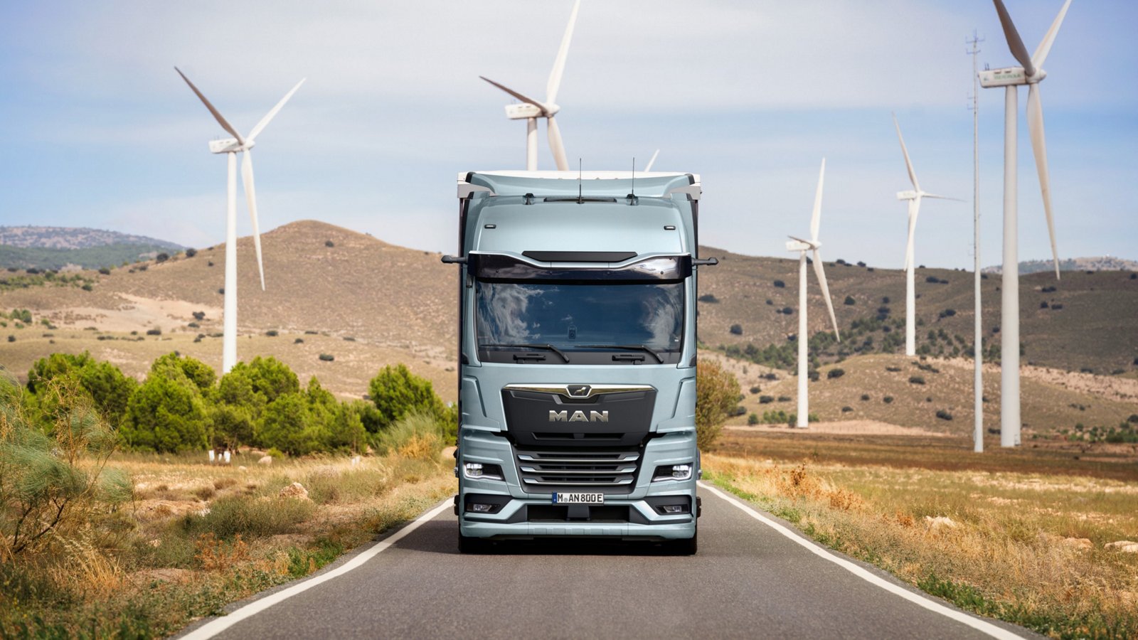 MAN eTruck driving through landscape with wind turbines in the background