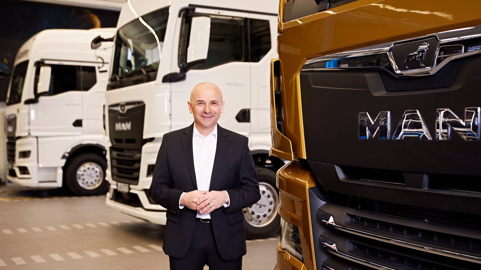 Murat Aksel, hands folded, standing in front of a row of trucks.