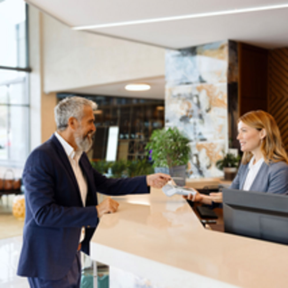 A man making a credit card payment at a hotel reception, tapping his card on a payment reader held by the receptionist.