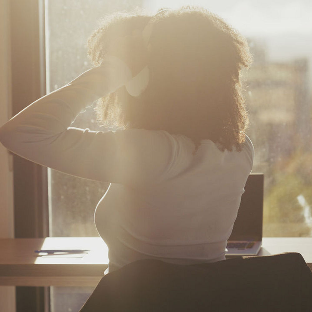 Woman with headphones on sat at a window desk looking outside.