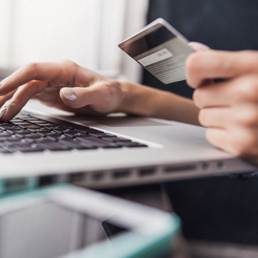 Person holding a credit card while typing on a laptop, appearing to make an online payment.