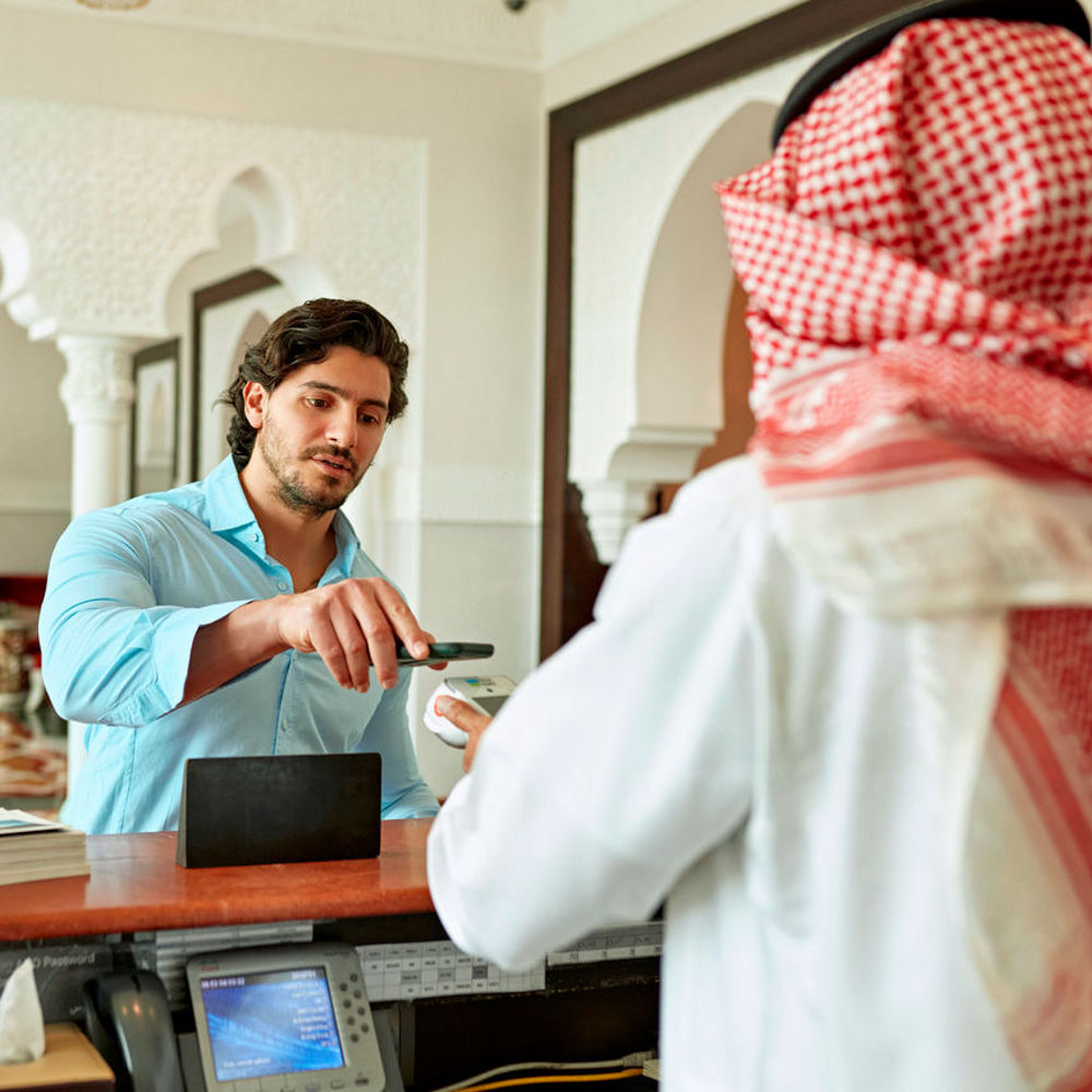 Man in a blue short is making a payment on a credit card at a hotel reception.
