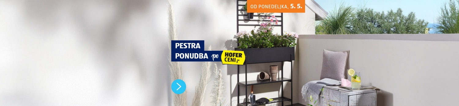 Balkon na katerem je prostor za sedeje z blazino in odejo, zraven je visoko črno stojalo z rožami in zelišči