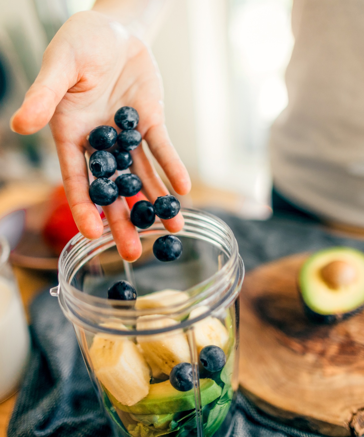 Eine Hand wirft ein paar Heidelbeeren in einen Mixer voller Obst.