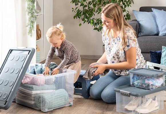 Deklica in mama pospravljata stvari v prozorne zaboje