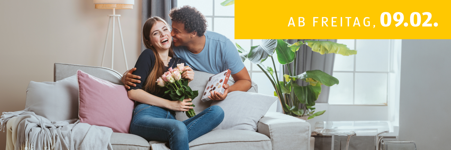 ab Freitag, 09.02. - Abgebildet sind eine Frau und ein Mann auf der Couch mit Valentinstags-Geschenken.