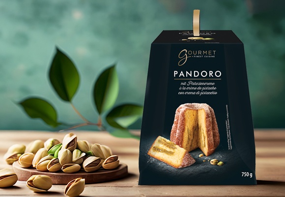 Pandoro s pistacijevim polnilom v črni škatli postavljen na mizi, poleg so pistacije