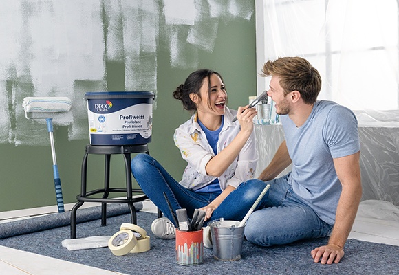 Moški in ženska sedita na tleh, okoli njiju je oprema za pleskanje