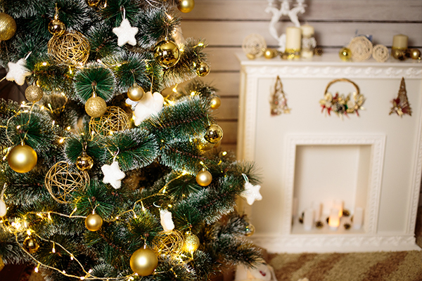 Christbaum ist weiß und golden geschmückt. Im Hintergrund ist ein dekorativer, weißer Kamin.