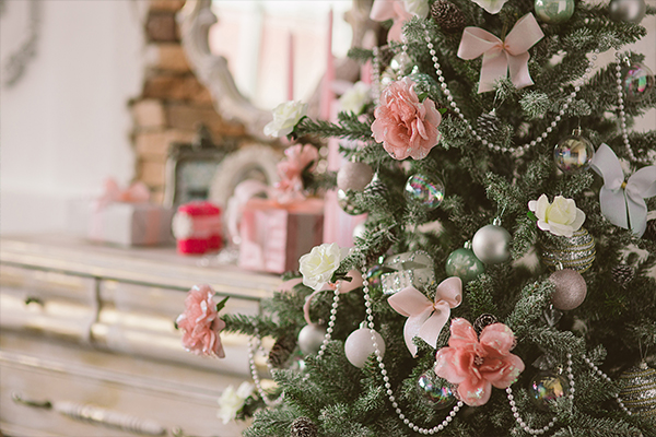 Ein lieblich geschmückter Christbaum mit rosa Blumen und Kugeln vor einem Schminktisch.