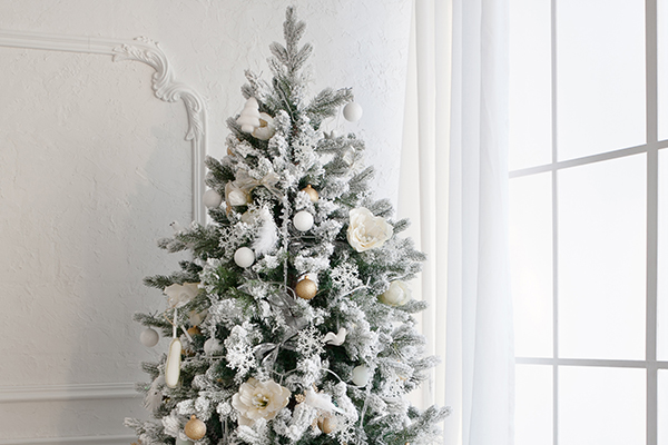 Christbaum mit weißer Dekoration und vor einer weißen Wand.