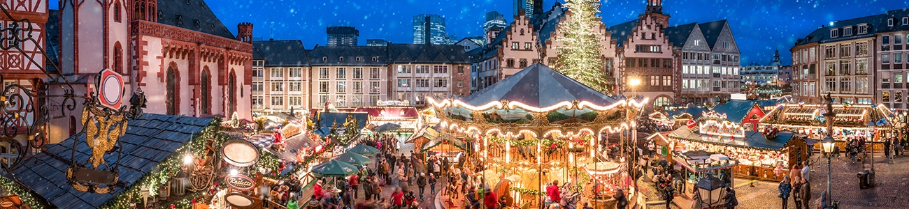 Draufsicht eines klassischen Christkindlmarktes mit vielen Lichtern, Ständen und Christbaum inmitten einer Altstadt.