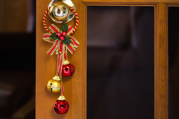 Rote und ein goldenes Glöckchen hängt auf einer Türklinke.
