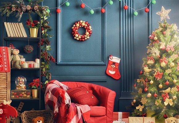 Weihnachtsdeko wie eine rote Socke, geschmückte Tannenzweige und ein Adventkranz hängen oder stehen vor einer blauen Wand.