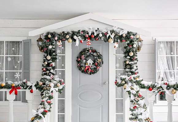Klassische Weihnachtsdekoration mit Tannenzweigen, Christbaumschmuck und Adventkranz an einer weiß-grauen Haustür von außen.