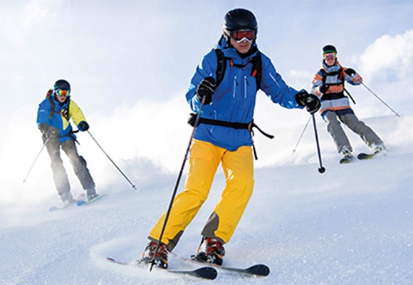 Drei Skifahrer mit Skibrille und Skihelm fahren einen schneebedeckten Hang herunter.