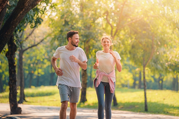 Ein Mann und eine Frau joggen durch einen Park mit grünen Bäumen.