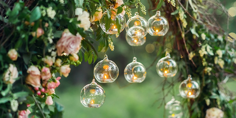 Brennende Teelichter hängen in einer Glaskugel unter einem Torbogen aus hellen Rosen.