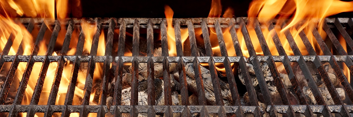 Ein Grillgitter unter dem brennende Kohlen zu sehen sind. Die Flammen reichen über das Grillgitter hinaus.