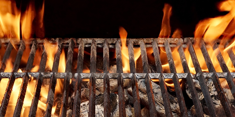 Ein Grillgitter unter dem brennende Kohlen zu sehen sind. Die Flammen reichen über das Grillgitter hinaus.