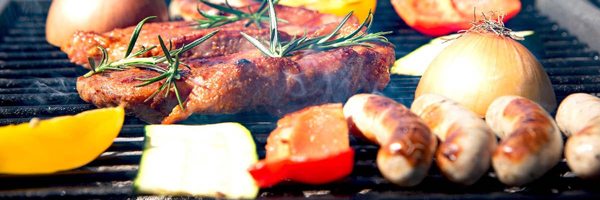 In Nahaufnahme werden Bratwürste, Steaks, Paprika, Zucchini und Zwiebel auf einem Rost gegrillt.