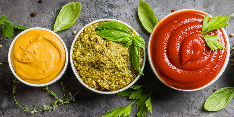 Drei Keramikschalen mit unterschiedlichen Dips und Soßen in Rot, Grün und Gelb.