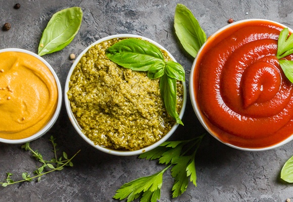 Drei Keramikschalen mit unterschiedlichen Dips und Soßen in Rot, Grün und Gelb.