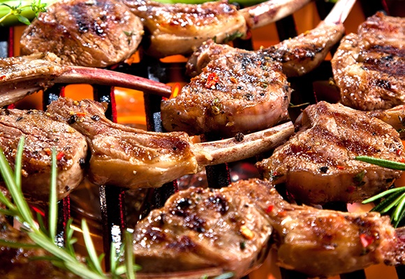 Lammfilet und Lammfleisch am Knochen liegt saftig und mit Streifen angegrillt auf einem glühenden Rost.