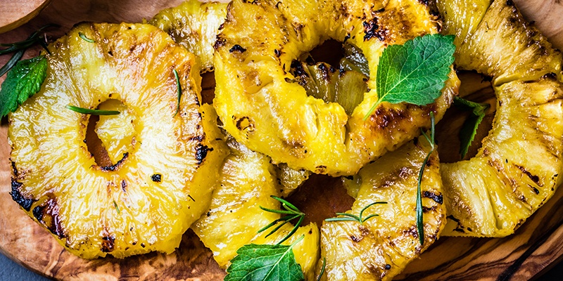 Mehrere gegrillte Ananas auf einem Holzbrett.