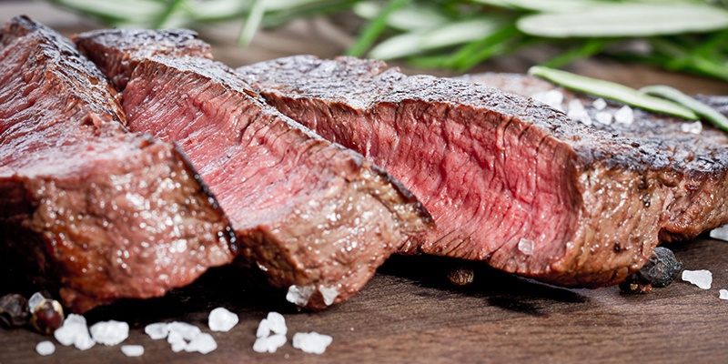 Ein in Scheiben geschnittenes Steak auf einem Holzbrett. Der Kern ist rosa.