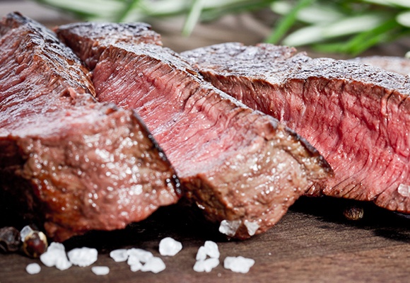 Ein in Scheiben geschnittenes Steak auf einem Holzbrett. Der Kern ist rosa.