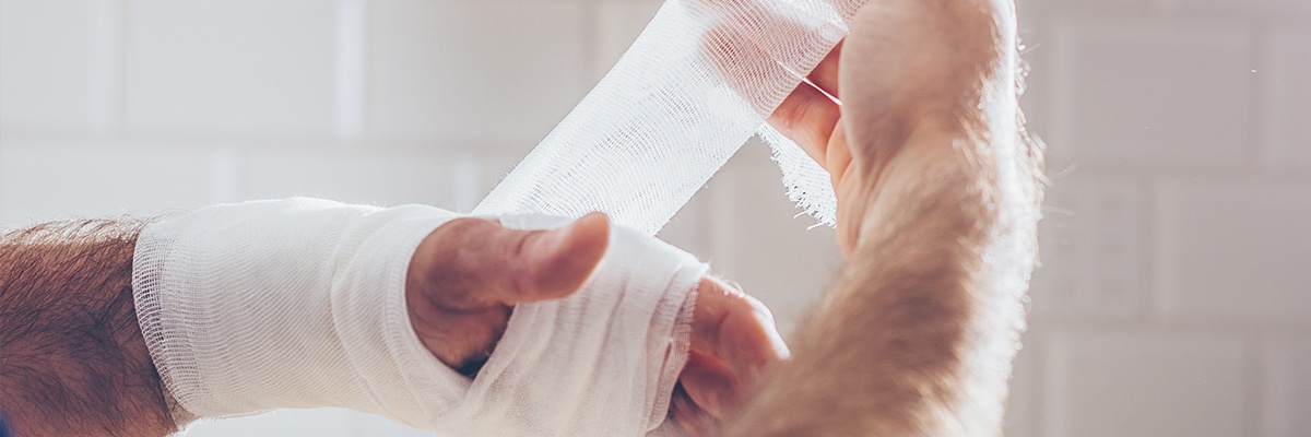 Zwei Hände eines Mannes. Mit der rechten Hand wickelt er sich um seine linke einen Verband.