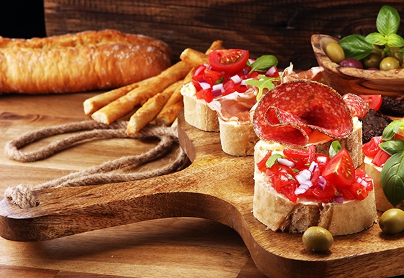 Ein Jausenbrett aus Holz auf dem mehrere mit Tomaten und Salami belegte Brötchen liegen. 