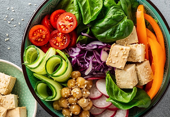 Eine grüne Schüssel mit Salat, Gurken, Tomaten, Kichererbsen, Radieschen und Tofuwürfel.