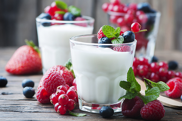 Drei Gläser mit Joghurt und Beeren stehen auf einem hölzernen Untergrund.