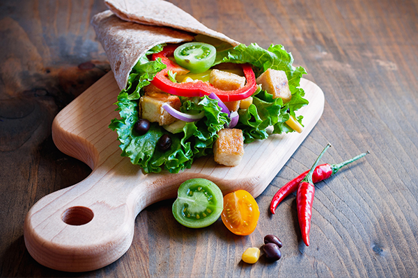 Auf einem Holzschneidebrett liegt ein vegetarischer Tortilla-Wrap.