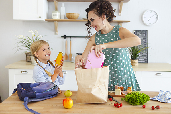 Eine Mutter und ihre Tochter stehen in der Küche und packen eine gesunde Jause in eine Papiertasche.