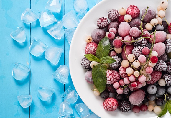 Ein Teller mit gefrorenen Beeren, daneben liegen Eiswürfel auf blauem Untergrund.