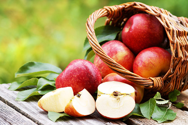 Ein Korb mit Äpfeln liegt auf einem Holztisch. Im Vordergrund ist ein Apfel in mehrere Spalten aufgeschnitten.