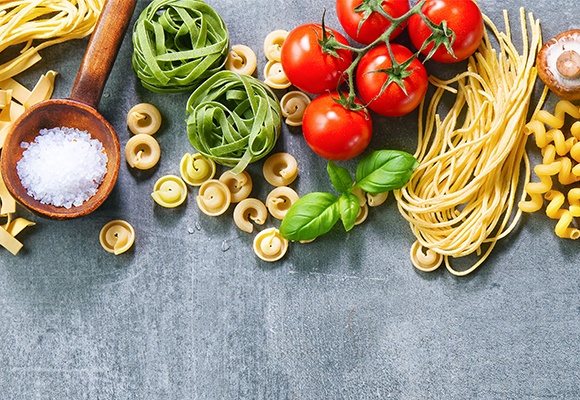 Unterschiedliche Sorten von Pasta liegen auf grauem Untergrund.