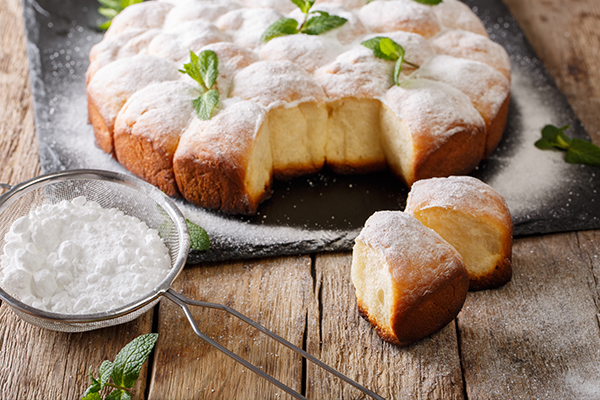 Selbstgemachte Buchteln mit Puderzucker auf einer grauen Steinplatte.
