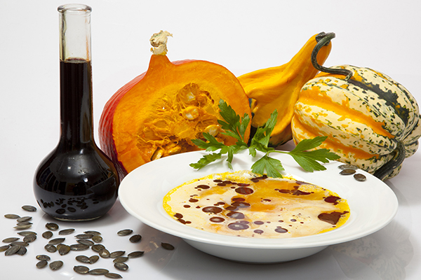 Eine Kürbiscremesuppe mit Kürbiskernöl in einem Suppenteller. Dahinter drei Kürbisse und eine Flasche Kürbiskernöl.